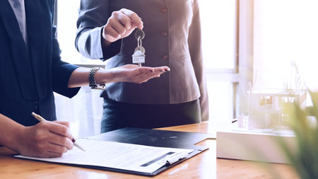 Real estate agent passing keys to a homeowner signing documents.